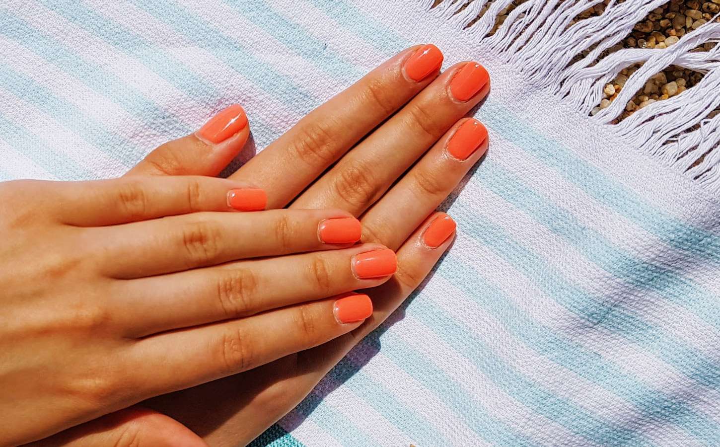 Hands with painted nails, resting on white beach towel.